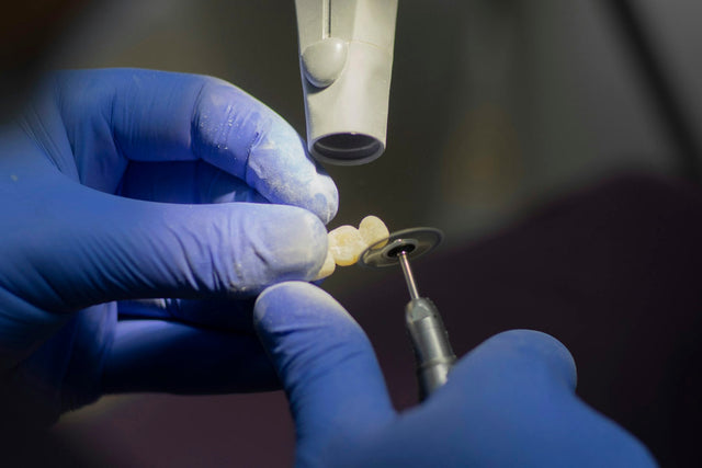 Gloved hand polishing a ceramic crown with a rubber wheel on a handpiece