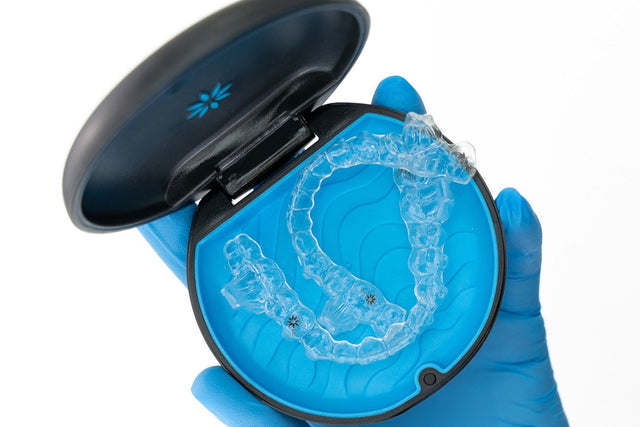 Clear dental appliance in its case, held in a gloved hand